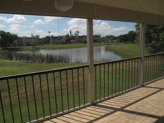 Panoramic view from a balcony overlooking a pond and surrounding greenery with buildings in the distance.