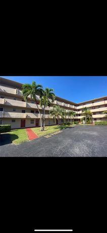 Front view of a multi-story apartment building with balconies and palm trees.