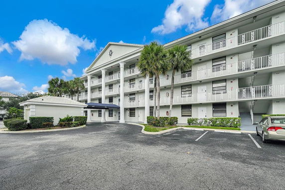 Front view of a multi-story residential building with balconies and a parking area in front.