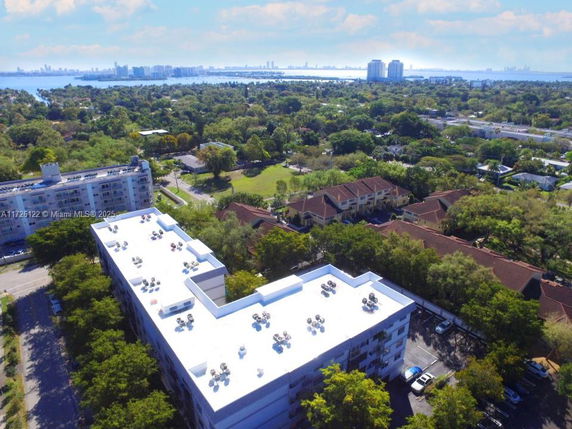 Aerial view of a residential area with a large building in the foreground and cityscape with water in the background.