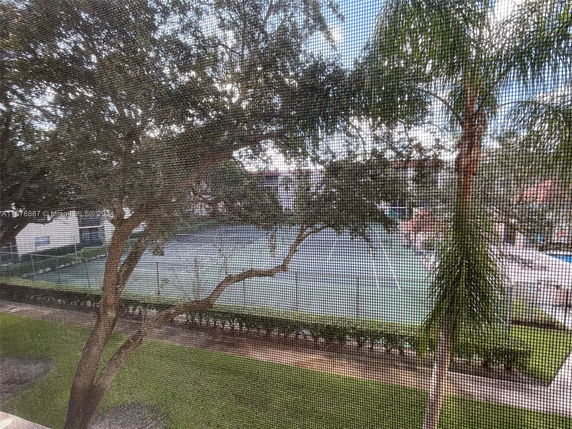 View of a tennis court surrounded by trees and a fence.