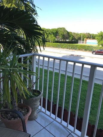 View from a balcony showing a road, greenery, and parked cars.