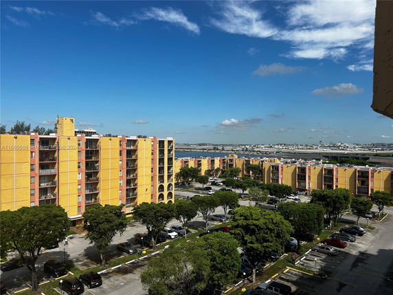 View of multiple mid-rise apartment buildings with yellow and orange exteriors, parking area, and surrounding landscape.