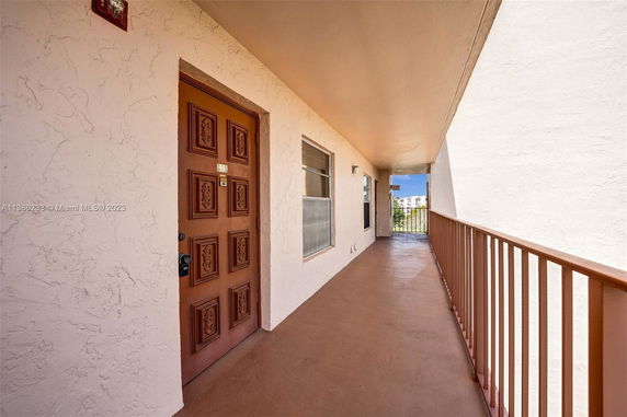 Exterior corridor of a building with a decorative brown door and railing.
