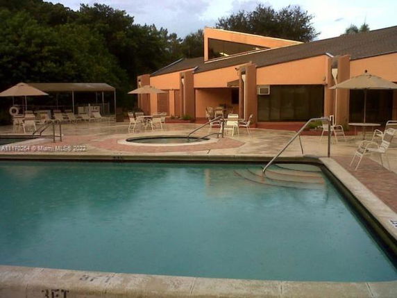 Outdoor swimming pool with patio chairs and umbrellas near a building.