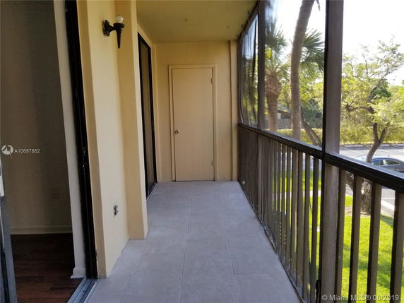 Balcony view with a screen enclosure overlooking trees and a parking area.