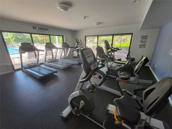 Room with exercise equipment including treadmills and stationary bikes facing windows.