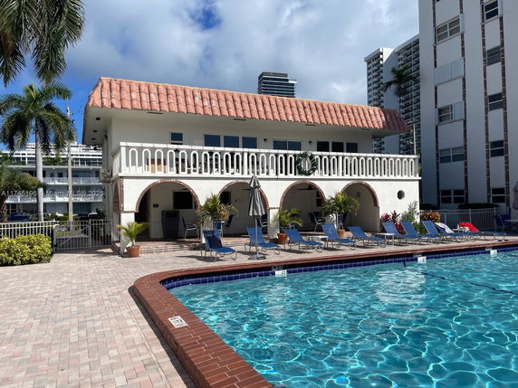 Outdoor area with a swimming pool and a two-story building featuring arches and a tiled roof.