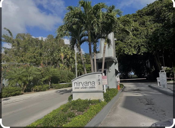 Entrance view of a residential complex with palm trees and a sign reading 'nirvana your urban oasis'.