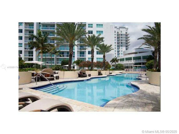 Outdoor swimming pool in a residential complex with palm trees and lounge chairs.