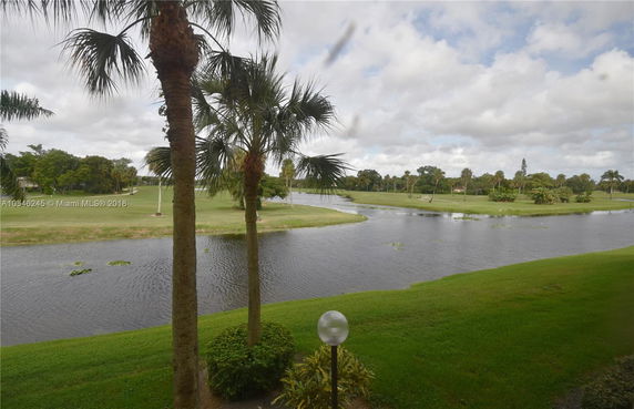 View of a golf course with a water feature and palm trees.