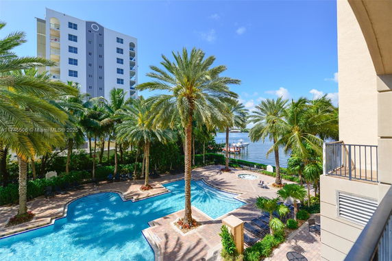 Outdoor swimming pool area with palm trees and a view of a high-rise building.