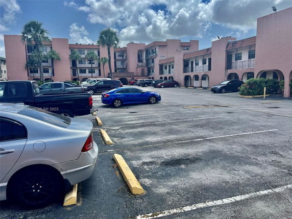 Outdoor parking area in front of a multi-story building with multiple cars parked.