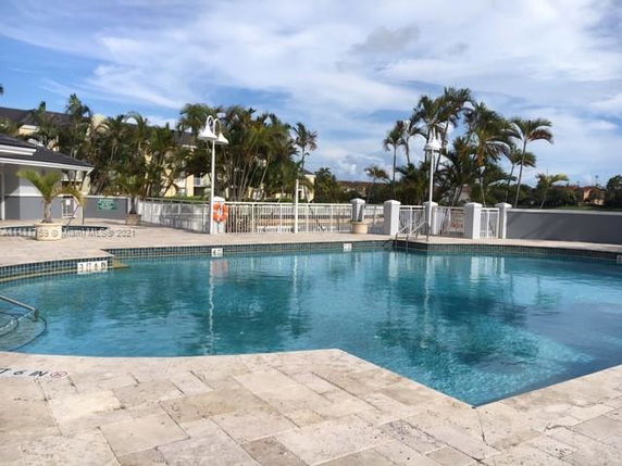 Outdoor swimming pool with surrounding fence and palm trees.