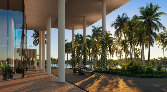 View from a building with tall columns and palm trees, overlooking a body of water.