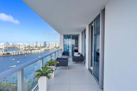 Balcony view of a waterfront cityscape with high-rise buildings and boats.