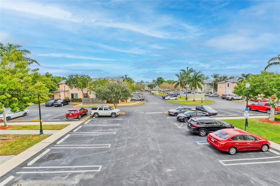 Outdoor parking area with multiple cars parked and apartment buildings in the background.
