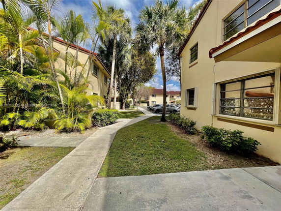 View of apartment buildings with sidewalks and palm trees.