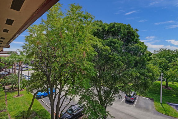 View of parking area with cars and greenery from a building.