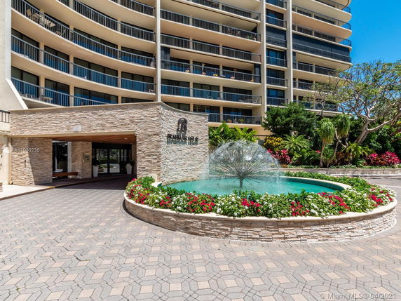 Front view of a multi-story building with curved balconies and a decorative fountain in front.