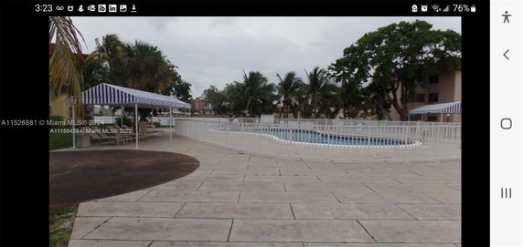 Outdoor swimming pool area with white fence and lounge chairs under striped canopies.