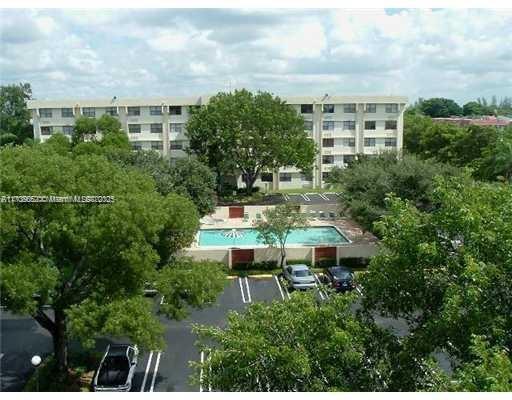 View of a multi-story apartment building with a swimming pool and surrounding trees.