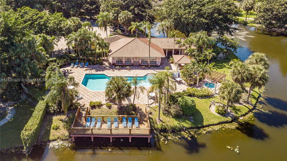 Aerial view of a house with a swimming pool, surrounded by lush greenery and adjacent to a body of water.