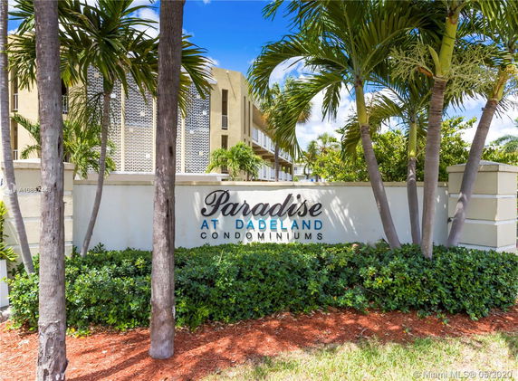 Front view of Paradise at Dadeland Condominiums with a sign and palm trees.
