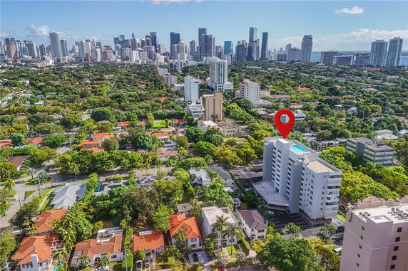 Aerial view of a cityscape with a tall building and surrounding greenery in the foreground.