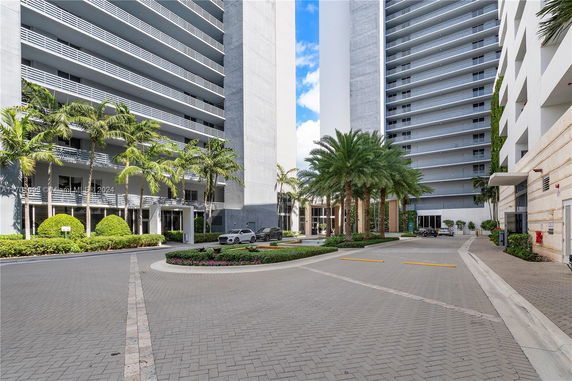 Front view of a multi-story building with balconies and palm trees at the entrance.