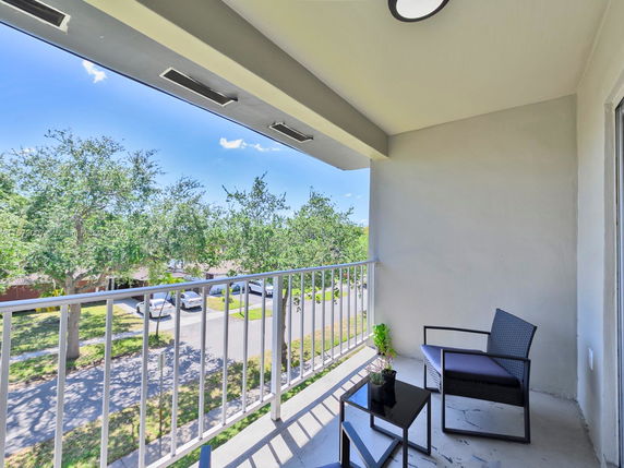 Balcony view with outdoor seating overlooking trees and street.
