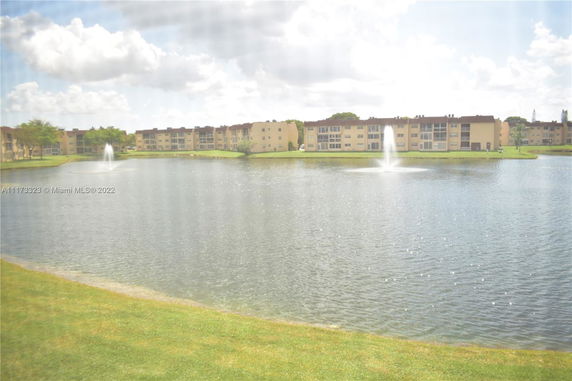 View across a lake towards a row of multi-story residential buildings with fountains in the water.