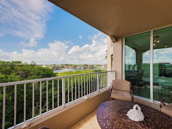 Balcony view overlooking lush greenery and a distant waterway, next to a partial glass door view into a room.