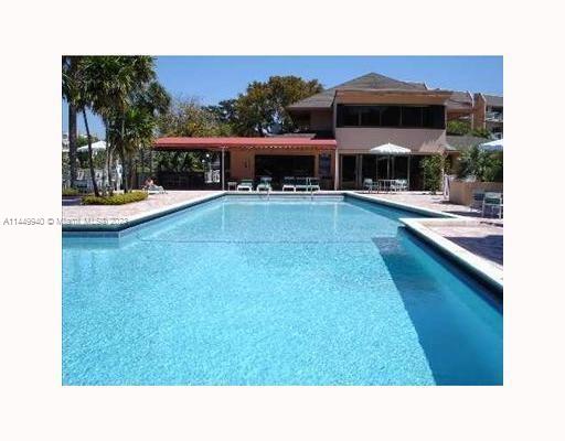 Outdoor swimming pool adjacent to a building with palm trees and sun loungers.