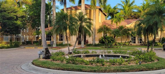 Front view of a house with a red-tiled roof and palm trees in front.