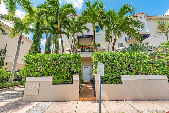 Front view of a multi-story house with a balcony and lush greenery.
