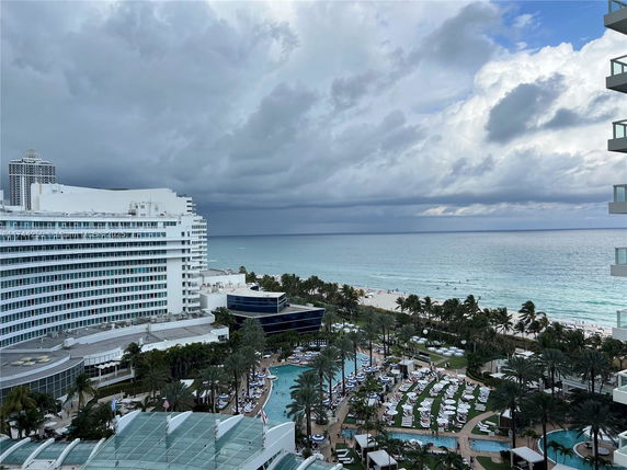 Scenic view of a large hotel near a beach with a swimming pool area and ocean in the background.