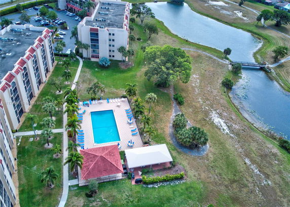Aerial view of a residential complex with a swimming pool and surrounding green spaces next to a pond.