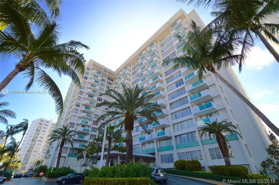 Front view of a tall residential building with balconies and palm trees.