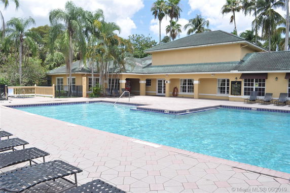 Outdoor swimming pool with adjacent building and palm trees.