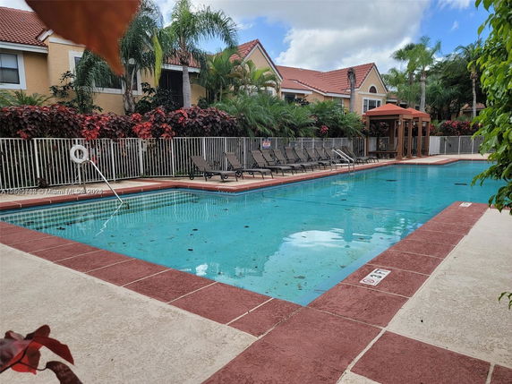 Outdoor swimming pool area with lounge chairs and fenced surroundings.