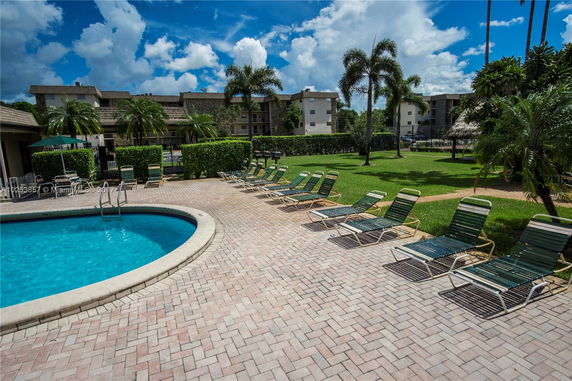 View of an apartment complex with a swimming pool and lounge chairs in the foreground.