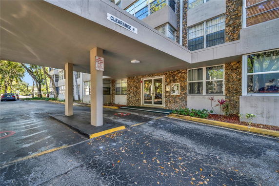 Covered parking area under a building entrance with stone façade and clearance sign.