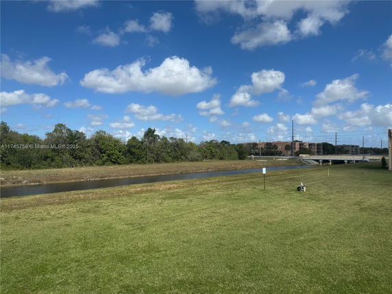 Expansive view of grassy area with a water body and distant buildings.
