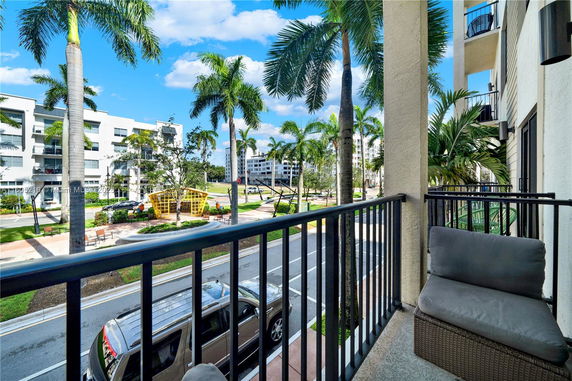 View from a balcony overlooking a street lined with palm trees and modern buildings.