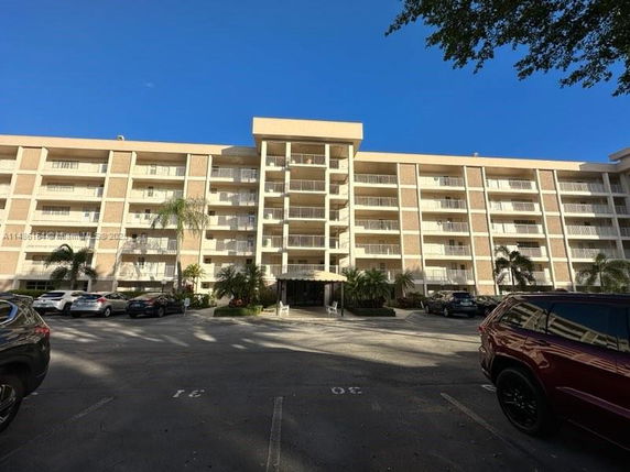 Front view of a multi-story residential building with balconies and parked cars.