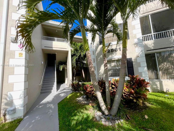 Front view of a two-story building with stairs leading to the entrance and surrounded by vegetation.
