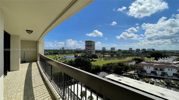 Panoramic view from a balcony showcasing a cityscape with multiple buildings and a green landscape.