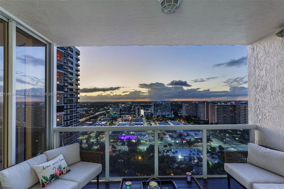 Panoramic view from a balcony showing a cityscape at dusk with buildings and lights.