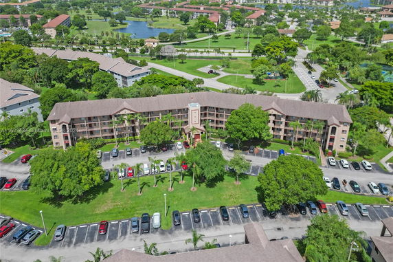Aerial view of a multi-story residential building with a parking lot and a landscaped area.